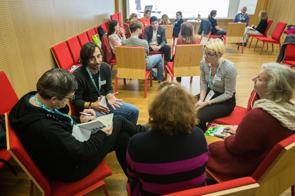 A teacher’s group during workshops. In the foreground there is a group of five people, discussing. Three other groups are sitting in circles in the background