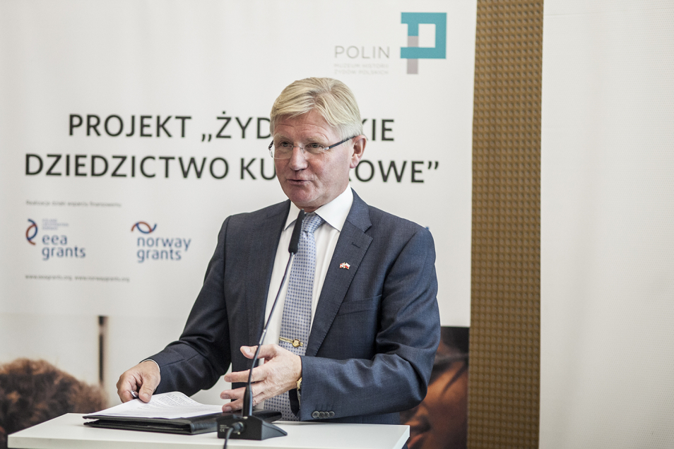Mężczyzna w okularach i garniturze. W tle baner z napisem projekt Żydowskie Dziedzictwo Kulturowe.