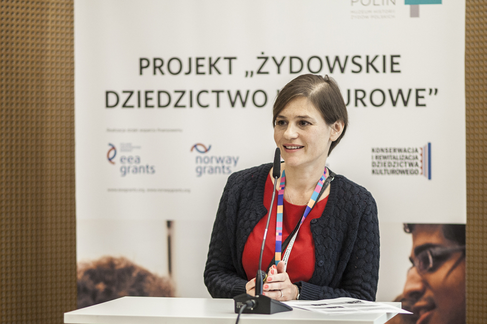 Kobieta stoi na tle planszy projekt "Żydowskie Dziedzictwo Kulturowe".