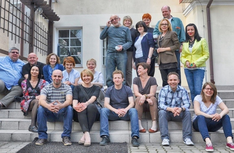 Grupa ludzi siedzi na schodach przed budynkiem.