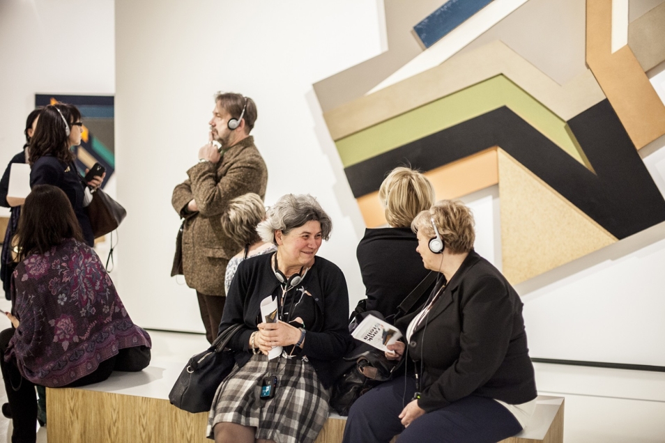 Ambasadorki i Ambasadorzy Muzeum POLIN rozmawiają, siedząc na ławeczce w przestrzeni wystawy "Frank Stella i synagogi dawnej Polski"