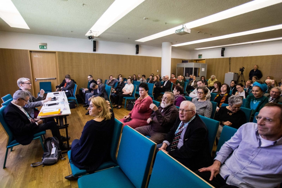 Przy stole siedzą od lewej: Jaff Schatz i Łukasz Bertram. Pozostałą część kadru wypełniają uczestnicy konferencji, którzy siedzą na krzesłach