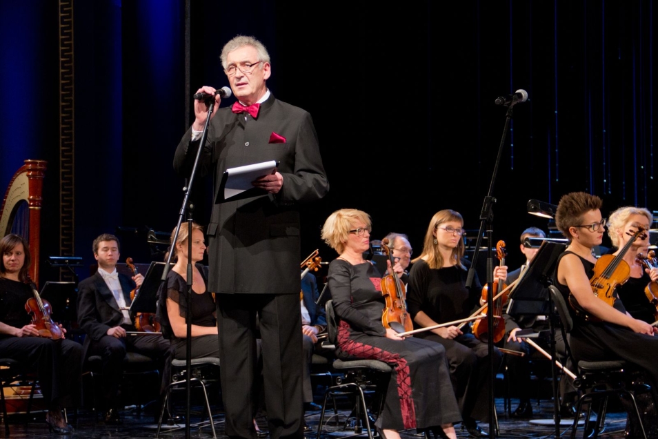 Gala w Teatrze Wielkim-Operze Narodowej. Mężczyzna stoi przy mikrofonie. W tle orkiestra.