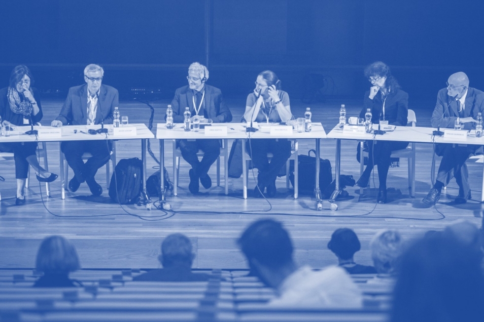 Grupa prelegentów siedzi przy stole podczas konferencji.