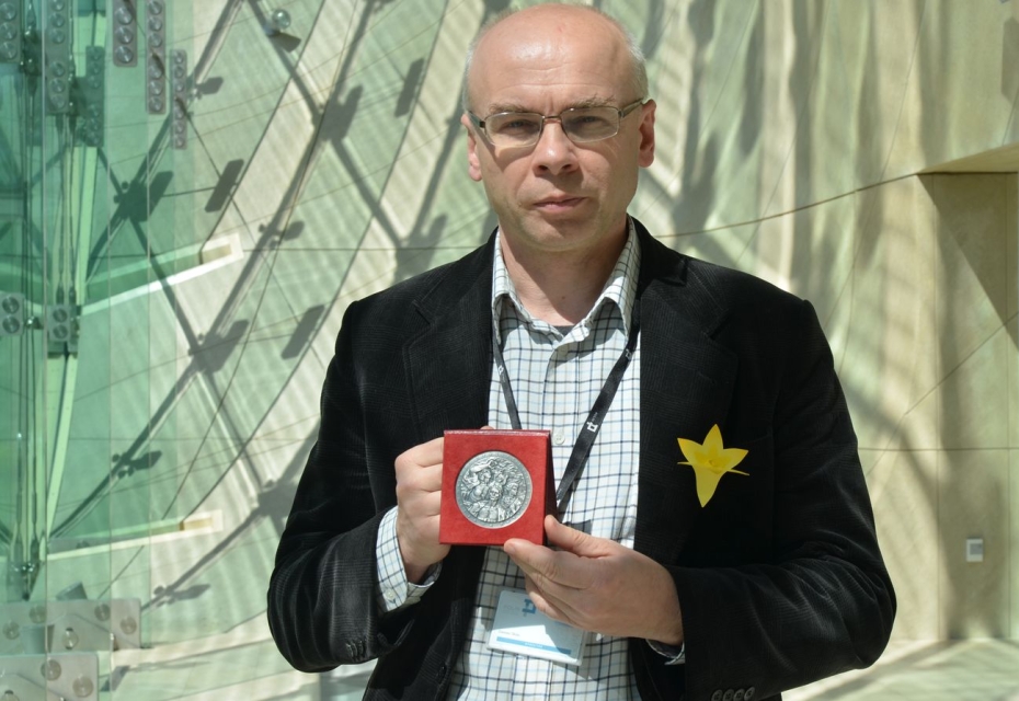 Dariusz Stola trzyma w rękach medal i pokazuje go. Wnętrze Muzeum Polin.