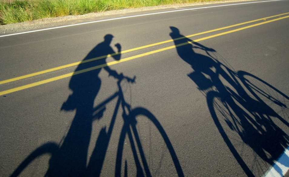 Cienie dwóch rowerzystów odbijają się na drodze.