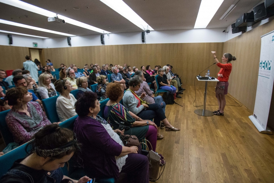 Sala wykładowa, przed słuchaczami stoi Gabriela Safran, profesor Uniwersytetu Stanforda.
