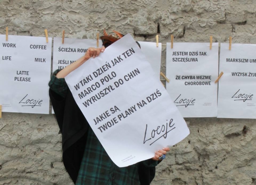 Ktoś trzyma jeden z plakatów Loesje. W tle na sznurku wiszą inne prace.