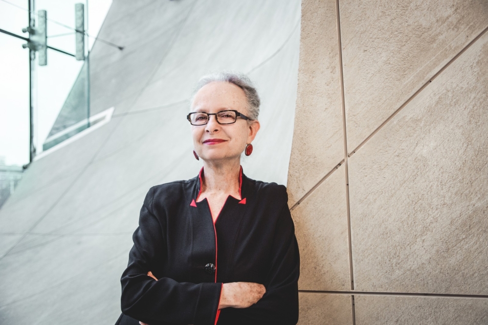 Prof. Barbara Kirshenblatt-Gimblett stoi oparta o ścianę muzeum w kolorze piasku pustyni