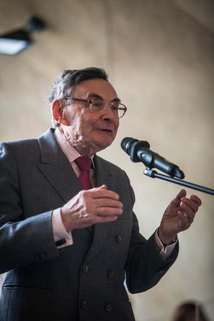 Marian Turski stoi przy mikrofonie.