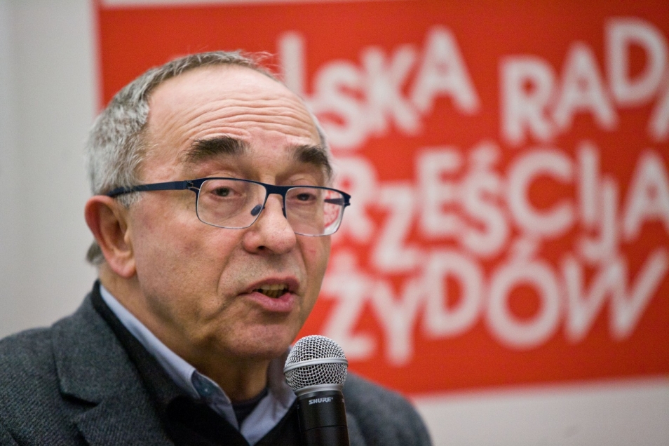 Mężczyzna w okularach mówi do mikrofonu. 