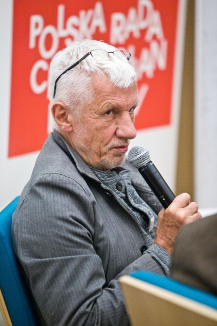Starszy mężczyzna mówi przez mikrofon podczas dyskusji "Uwierzyć w muzeum".