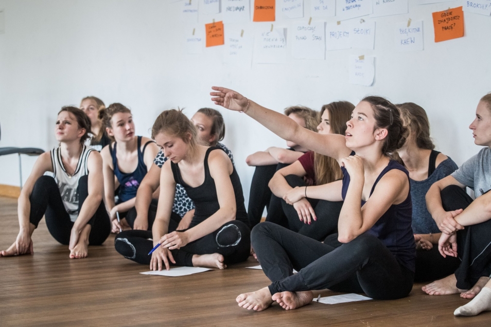 Grupa młodych kobiet siedzi na podłodze podczas warsztatów teatralnych.