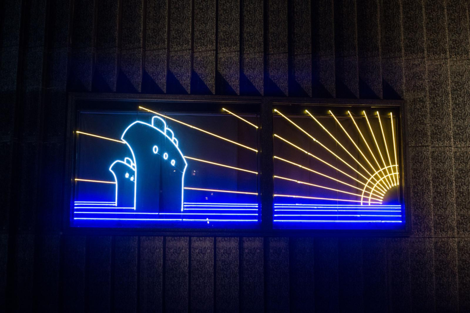 Neon przygotowany na wystawę "Gdynia - Tel Awiw", przedstawia statki dalekomorskie na wodzie, nad horyzontem po prawej stronie słońce, którego promienie rozciągają się na całe tło neonu, autor: Maurycy Gomulicki
