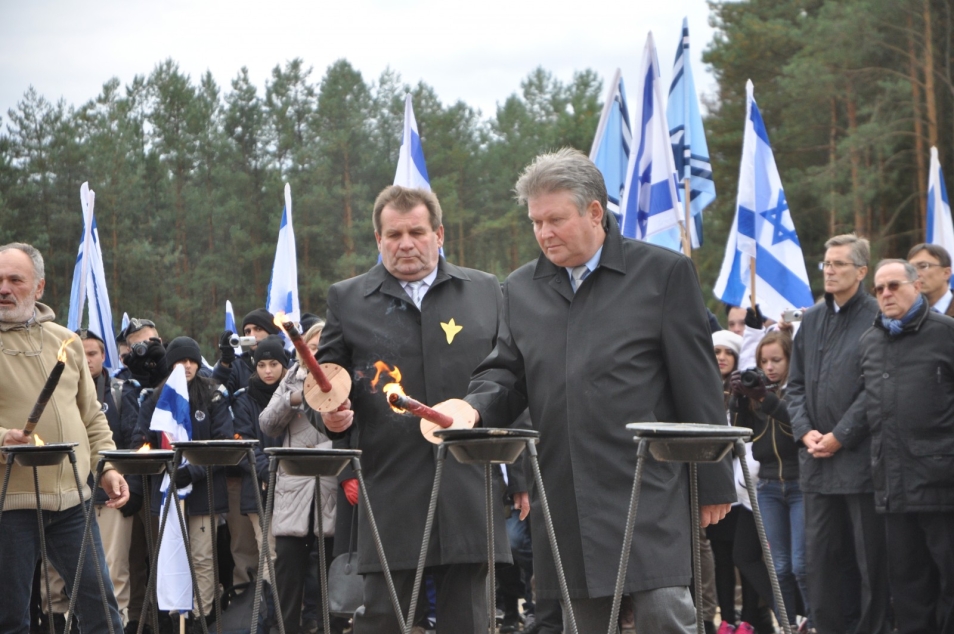 Dwóch mężczyzn zapala pochodnie. W tle flagi izraelskie.