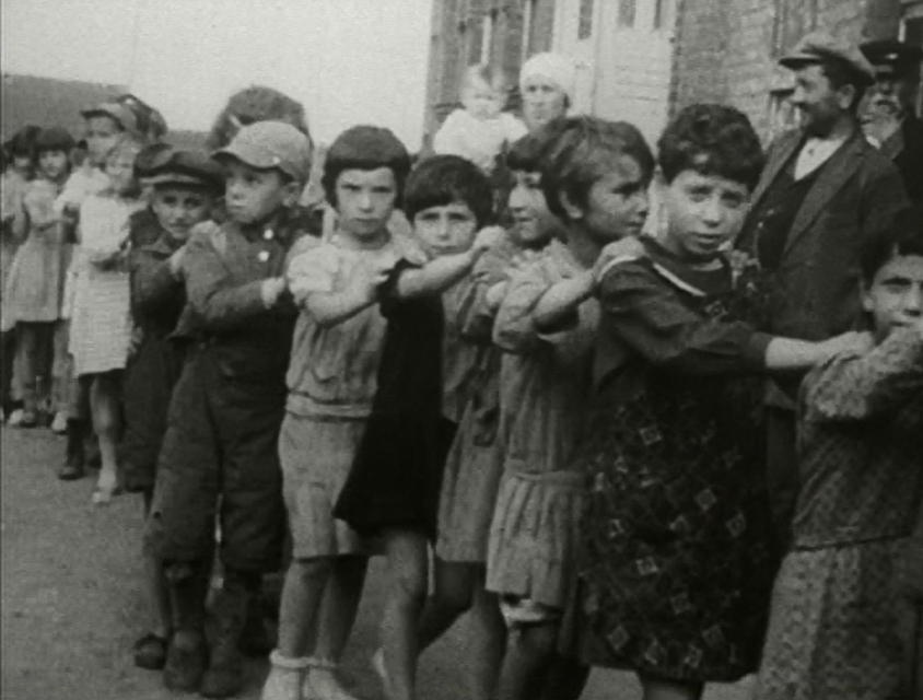 Grupka chłopców stoi w wężyku - każdy kładzie kolejnemu dłonie na ramionach.