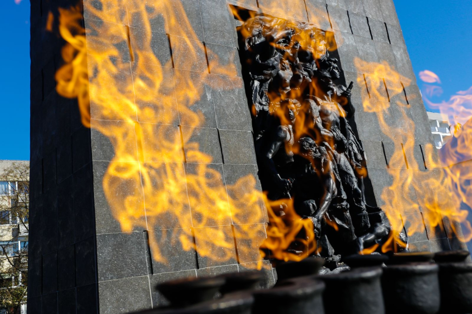Pomnik Bohaterów Getta - duży monument z granitu z rzeźbionymi postaciami Żydów z getta warszawskiego, widziany zza płomieni palących się przed nim zniczy