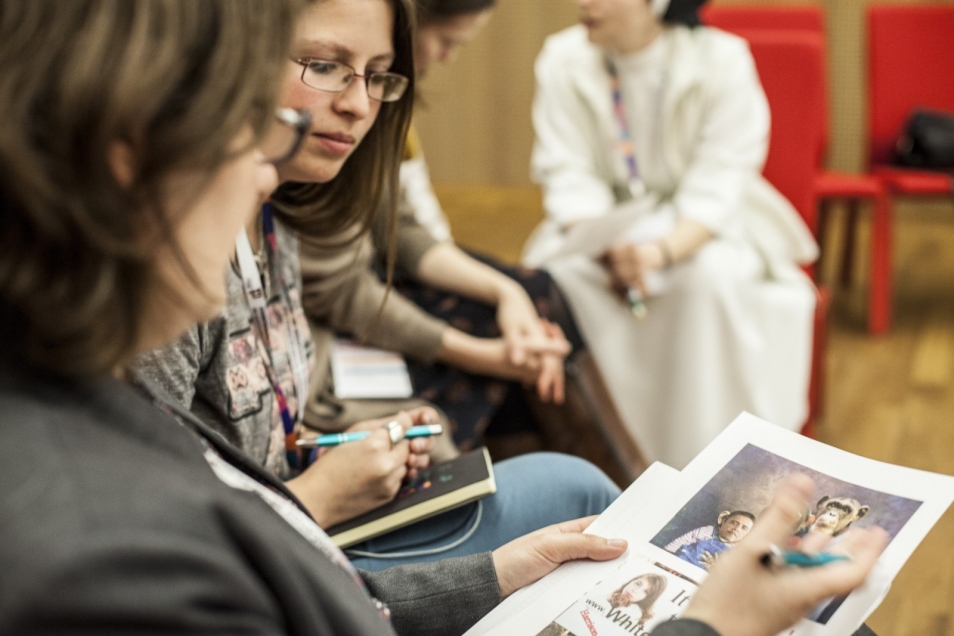 Warsztaty edukacyjne dla szkół ponadpodstawowych. Trzy kobiety, które dyskutują nad zdjęciami wydrukowanymi na kartkach, które trzyma jedna z nich.