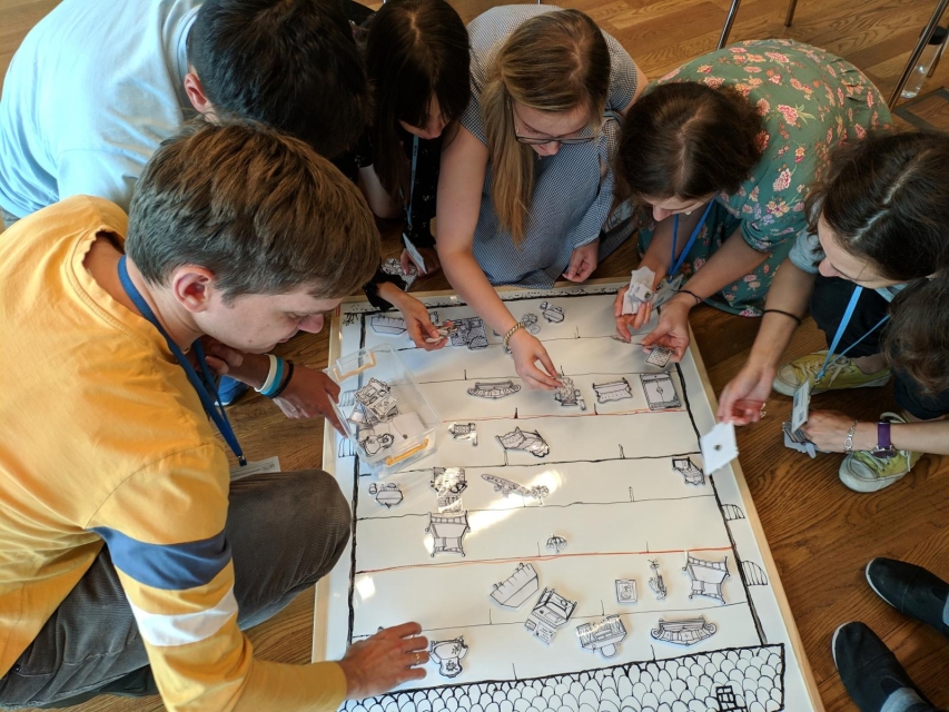 Podsumowanie projektu "EDU-NET: EAST. Przez edukację nieformalną do nowych liderów”. Na zdjęciu: uczestnicy programu podczas warsztatów - pochylają się nad rozłożoną na podłodze planszą