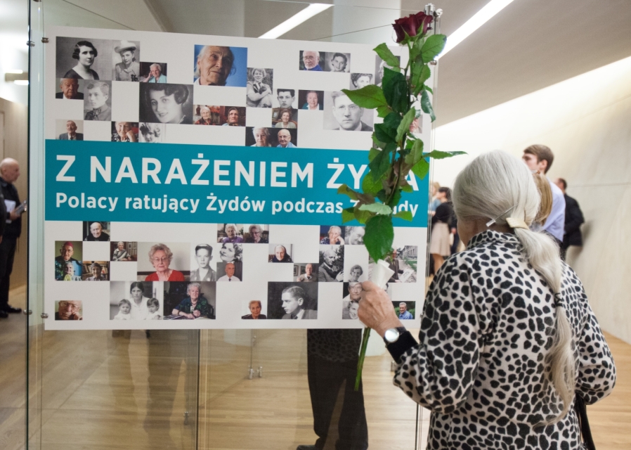 Kobieta ogląda wystawę o Sprawiedliwych, w jednej dłoni trzyma różę.