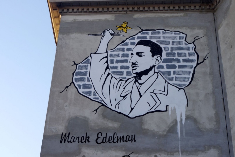 Mural przedstawiający młodego Marka Edelmana, ujęty z profilu, sylwetka od pasa w górę, w uniesionej prawej dłoni ściska żółtego żonkila. Mural wykonany przez D. Paczkowskiego na ścianie szkoły przy ul. Karmeliskiej w Warszawie - ilustracja warsztatów dla uczniów klas 7-8 szkół podstawowych w Muzeum POLIN