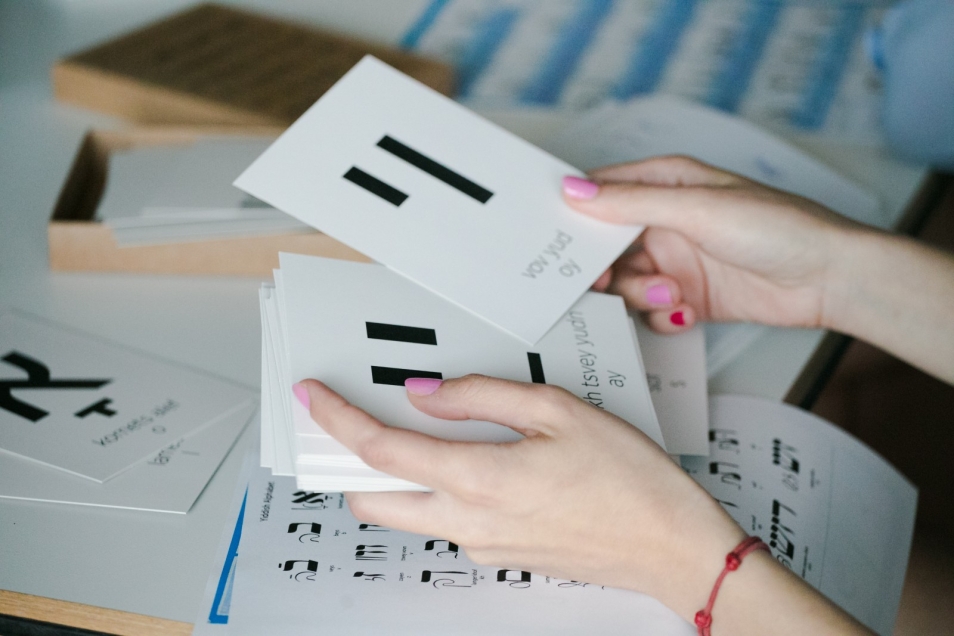 Warsztaty edukacyjne dla szkół ponadpodstawowych. Na zdjęciu widać dłonie, które trzymają duże białe karty z czarnymi hebrajskimi literami - po jednej literze na karcie