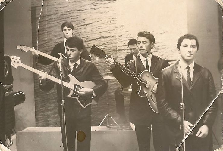 Czarno-białe zdjęcia przedstawia mężczyzn z gitarami stojących na scenie.