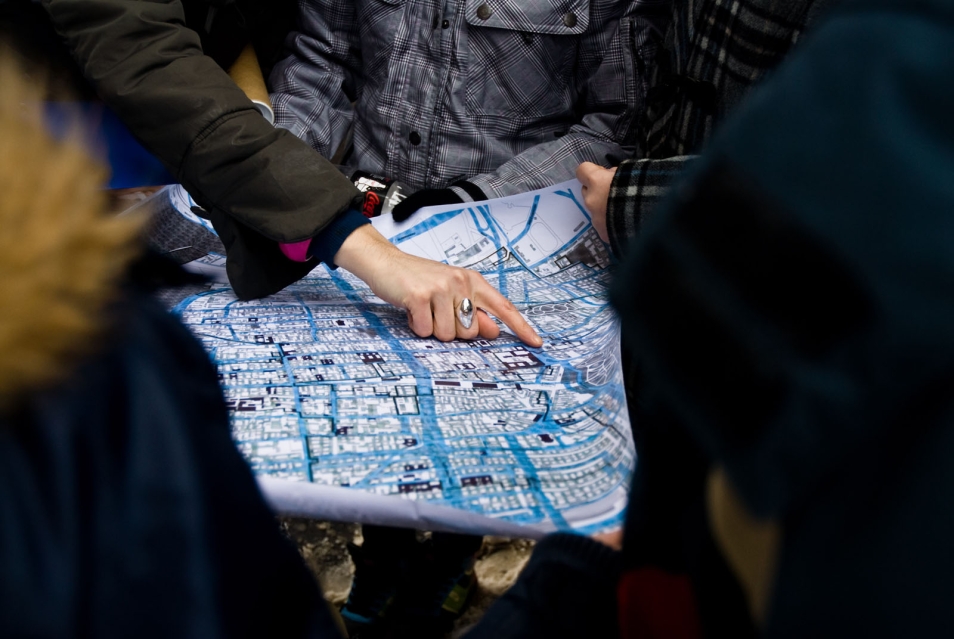 Kilka osób trzyma mapę Muranowa. Ktoś wskazuje jakiś punkt na mapie.