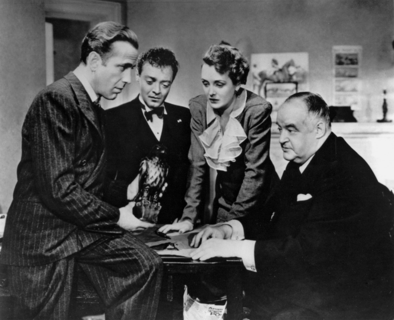 Kadr z filmu "Sokół maltański". Trzech mężczyzn i kobieta skupieni, pochylają się nad czymś.