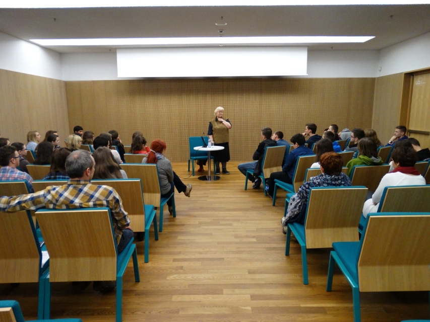 Wykład. Sala pełna ludzi. Prowadzący stoi przed grupą.