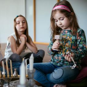 Trzy dziewczynki siedzą na podłodze przy świecznikach. Jedna z nich trzyma drejdel - bączek do gry.