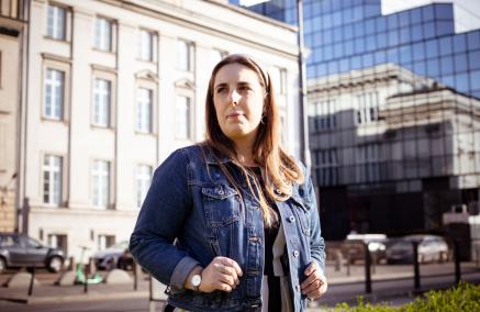 Katarzyna Jankowska - przewodniczka Muzeum POLIN - na placu Bankowym w Warszawie. W tle jedna z kamienic i błękitny wieżowiec.