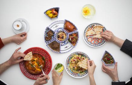 Kilka osób sięga do talerzy z daniami kuchni żydowskiej - pitą, hummusem, gołąbkami, sałatką izraelską.