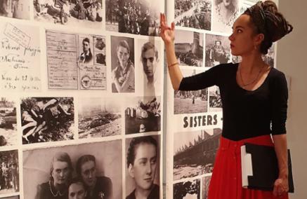 Zuzanna Hertzberg wskazuje dłonią zdjęcie na planszy na wystawie "Bojowniczki. Archiwum afektywne".