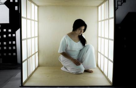 Instalacja Hany Umedy pt. "Endless box". W środku oświetlonego pudełka siedzi ciemnowłosa ubrana na biało kobieta.