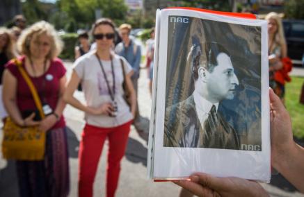 Ktoś trzyma czarno-biały portret Juliana Tuwima. W tle grupa uczestników spaceru miejskiego.