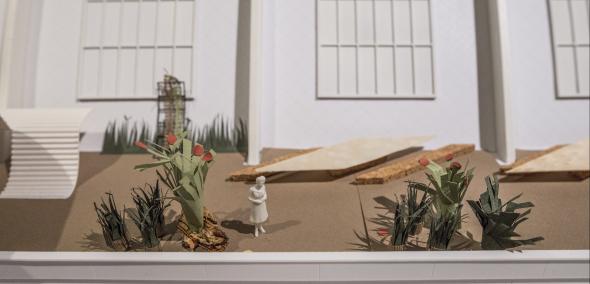 Widok na jedną z makiet z wystawy "Gdynia - Tel Awiw", zhakowaną podczas interwencji artystycznej - do makiety został dodany piasek, ławeczki, postać kobiety i rośliny
