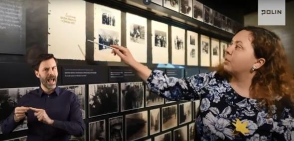 Na zdjęciu po prawej stronie kobieta - Anita Borkowska, przewodniczka Muzeum POLIN - pokazuje na jedną z grafik, widoczną na ścianie po lewej stronie kadru. W lewym dolnym rogu widać tłumacza PJM