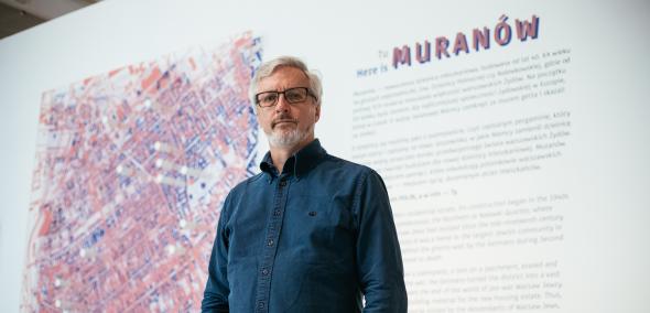 Przed planszą któa otwiera wystawę Tu Muranów stoi mężczyzna - Jacek Leociak. Na planszy opis wystawy oraz mapa Muranowa