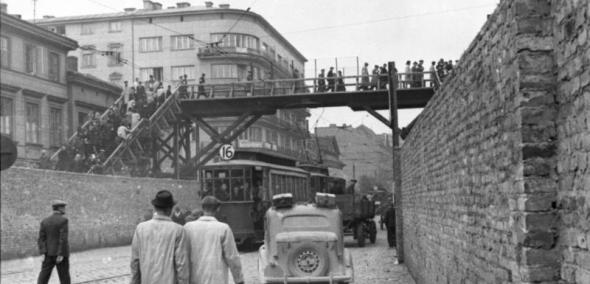 Na obrazie widzimy zdjęcie z warszawskiego Getta, dokładnie ulicę Chłodną (widok w kierunku zachodnim) przy skrzyżowaniu z ulicą Żelazną. Ulica była aryjska a ponad ulicą jest widoczny most łączący Małe i Duże Getto.