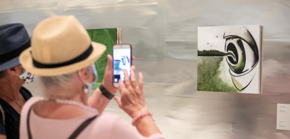 Na obrazie widzimy kobiety robiące zdjęcia jednej obrazom w sali wystawienniczej. 