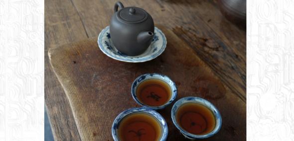 Na ciemnej desce ze starego drewna stoi czajniczek i czarki z herbatą