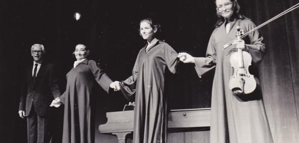 Czarno-biała fotografia. Lin Jaldati Ensemble 1984. Jeden starszy mężczyzna w garniturze i trzy kobiety w długich szatach stoją na scenie, trzymając się za ręce. Kobieta, która stoi z prawej strony, trzyma skrzypce.
