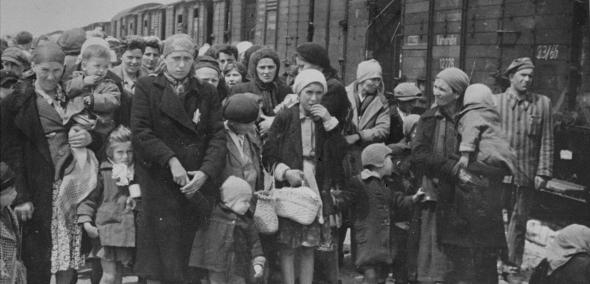 Grupa Żydów w różnym wieku stoi przy wagonach bydlęcych zmierzających do obozu zagłady.