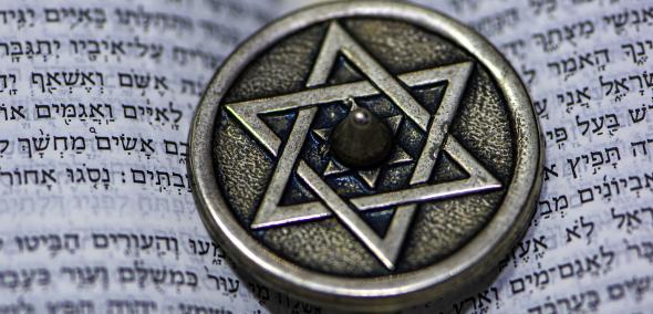 Na księdze w języku hebrajskim leży mały okrągły stalowy przedmiot z wyrytą na środku gwiazdą Dawida.