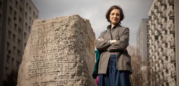 Przewodniczka Julia Chimiak stoi obok kamienia-pomnika z wyrytymi nazwiskami.