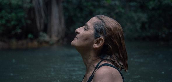 Kadr z filmu "Terytorium". Starsza kobieta stoi bokiem, unosząc lekko głowę. Otacza ją woda.