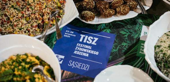 W miseczkach różne dania, a pomiędzy nimi okładka katalogu "Tisz - Festiwal Żydowskiego Jedzenia".