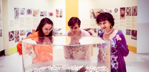 Trzy osoby oglądają eksponat prezentowany w gablocie na wystawie "Od kuchni" w Muzeum POLIN.