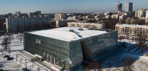 Budynek Muzeum POLIN z zewnątrz, pokazany z góry, z drona. W tle bloki i biurowce.